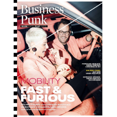 Zwei Personen in rosa Kleidung sitzen in einem Auto mit rotem Lederinterieur, eine Person hält das Lenkrad, die andere eine Zigarette.